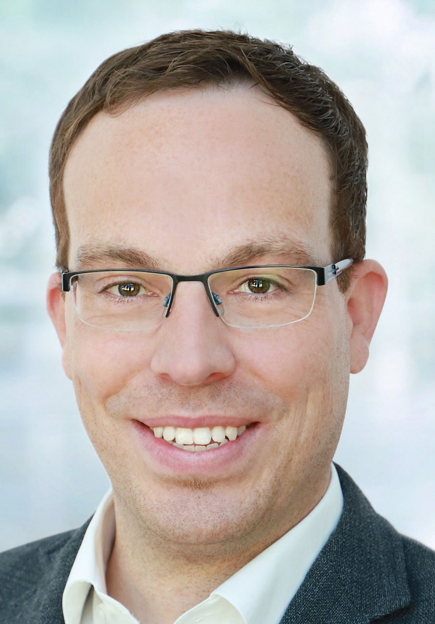 Mitarbeiter der Bank im Anzug und mit Brille lächelt in die Kamera.