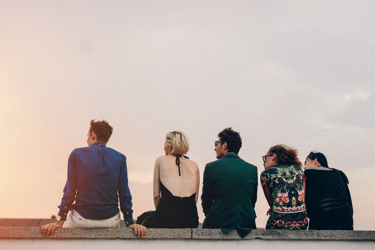 Fünf junge Menschen sitzen auf einer Mauer und schauen sich den Sonnenuntergang an