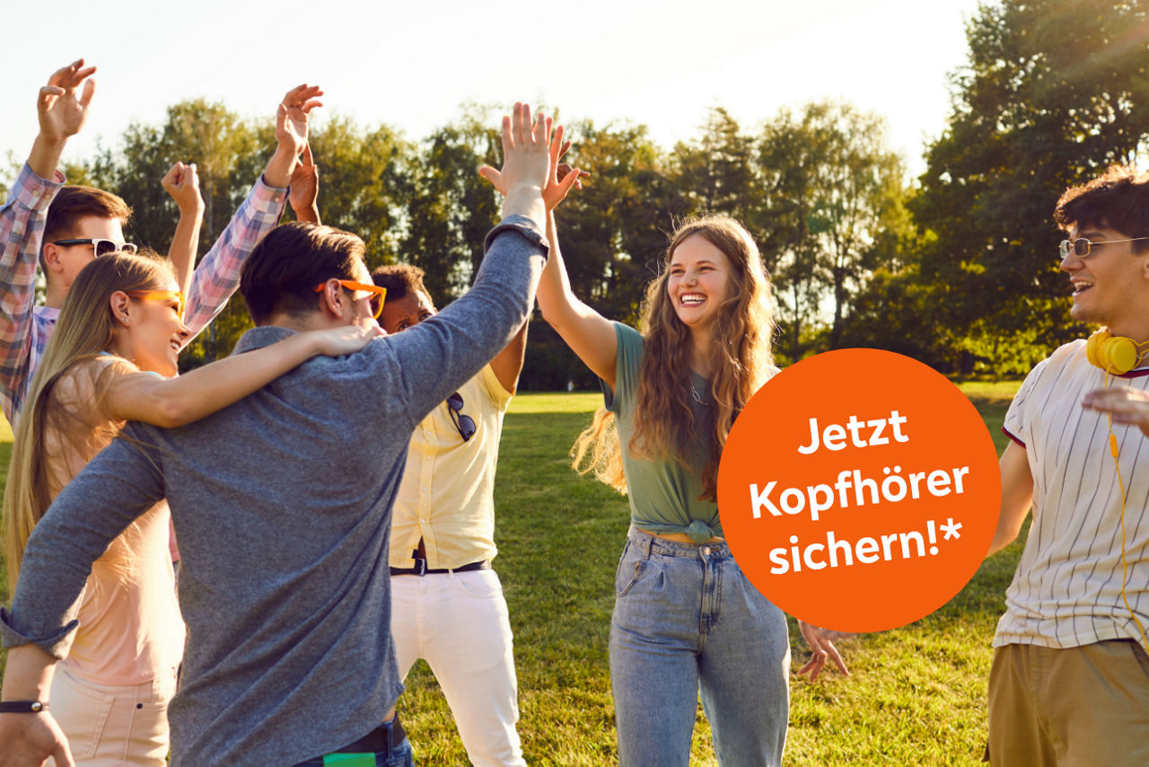 Mehrere junge Leute stehen auf einer Wiese und heben die Arme in die Luft.