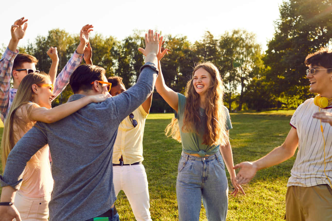 Mehrere junge Leute stehen auf einer Wiese und heben die Arme in die Luft.