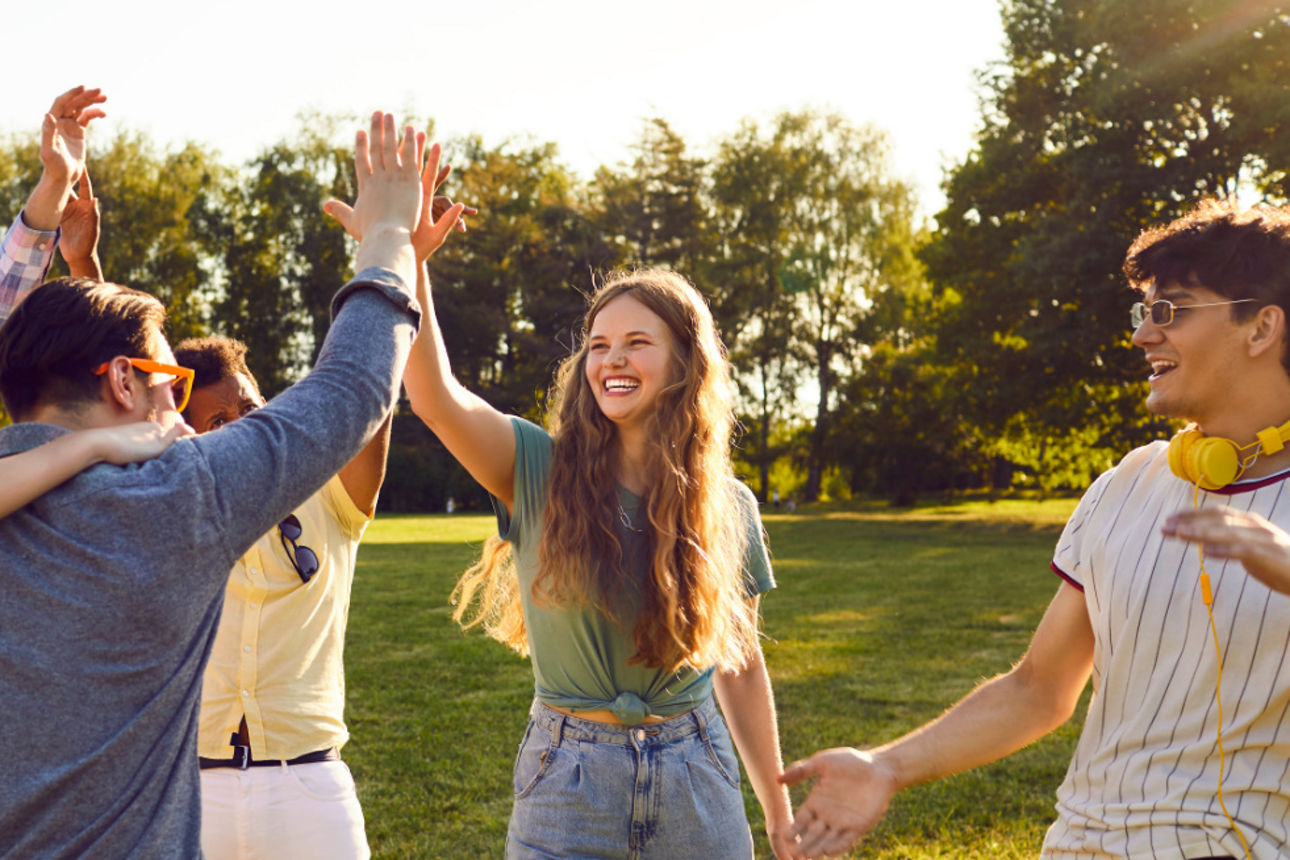 Mehrere junge Leute stehen auf einer Wiese und heben die Arme in die Luft.