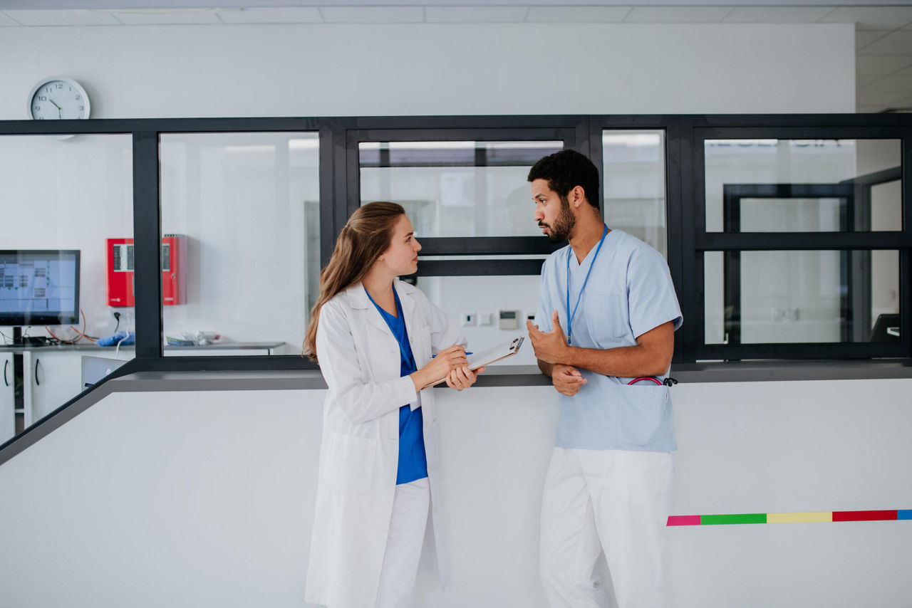 Junger Arzt spricht an der Krankenhausrezeption mit seiner Kollegin.