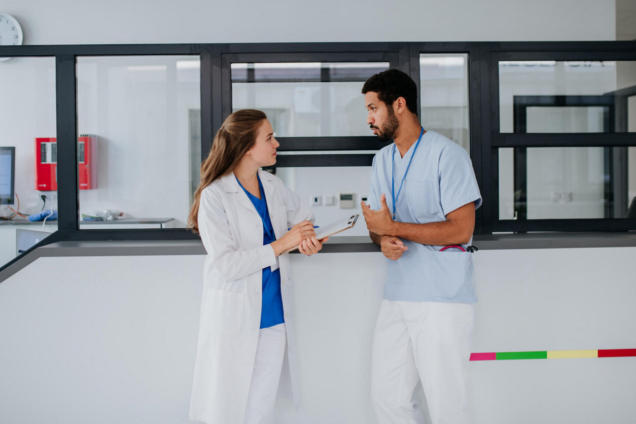 Junger Arzt im Gespräch an Krankenhausrezeption mit Kollegin.