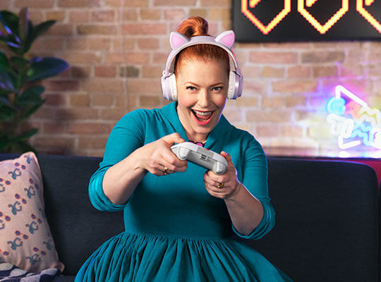 Eine Frau in einem türkisen Kleid spielt auf ihrer Couch ein Videospiel