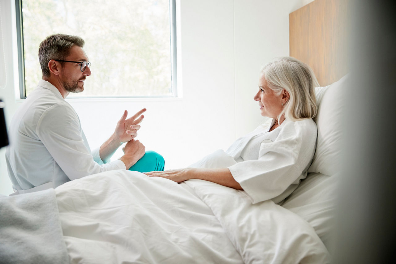 Arzt im weißen Kittel besucht reife Patientin im Krankenhausbett
