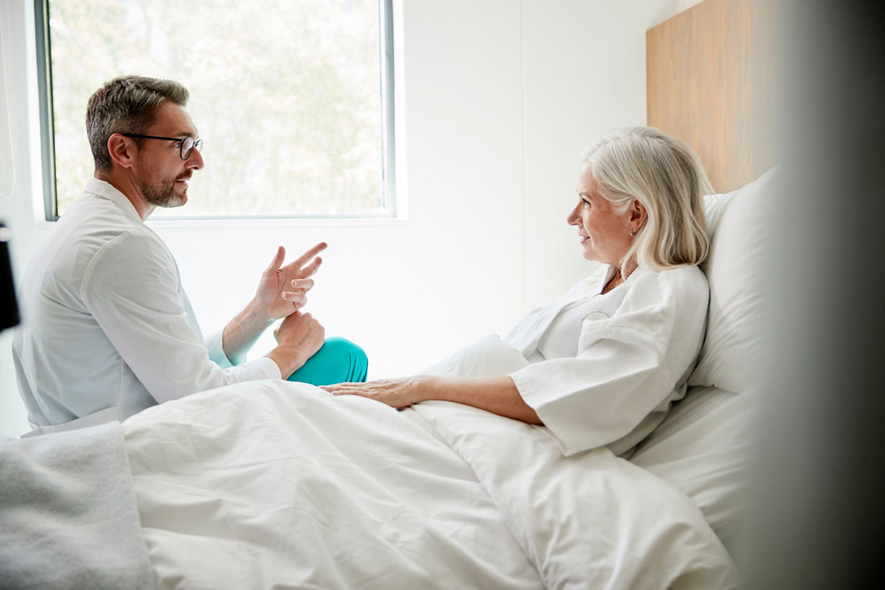 Arzt im weißen Kittel besucht reife Patientin im Krankenhausbett