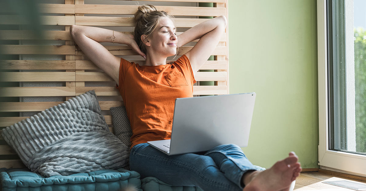 Frau sitzt mit Laptop auf Bett und entspannt sich