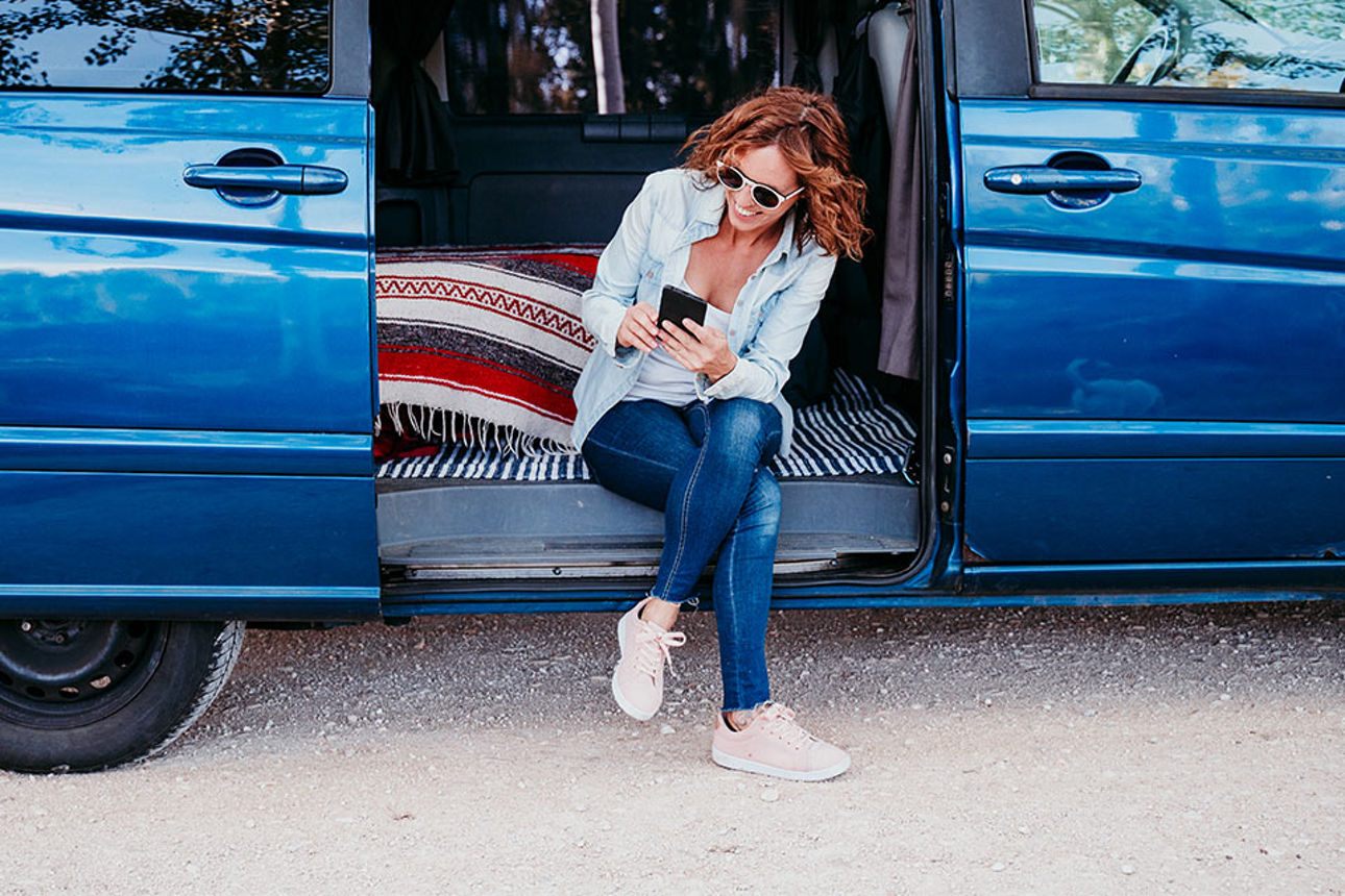 Junge Frau sitz im Auto und schaut auf ihr Mobiltelefon
