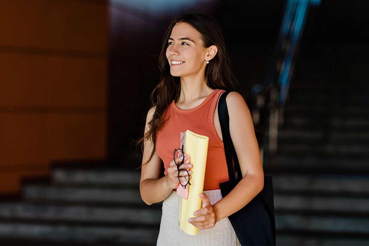 Lächelnde junge Frau mit Umhängetasche und gefalteten Unterlagen