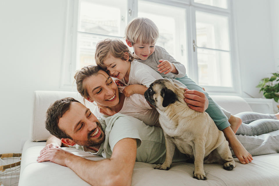 Eine glückliche Familie mit zwei Kindern und Hund liegt aufeinander gestapelt auf einem Bett.