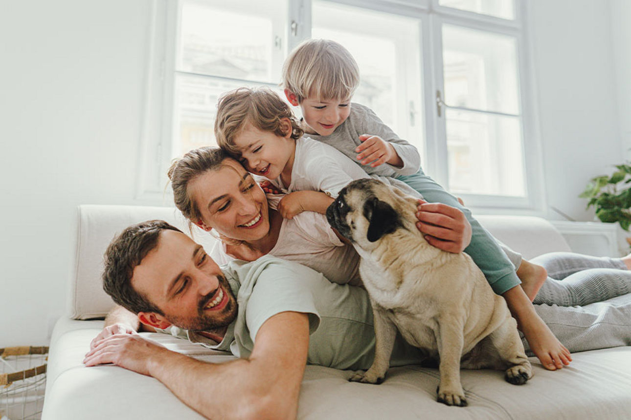 Glückliche Familie mit zwei Kindern und Hund liegt übereinandergestapelt im Bett