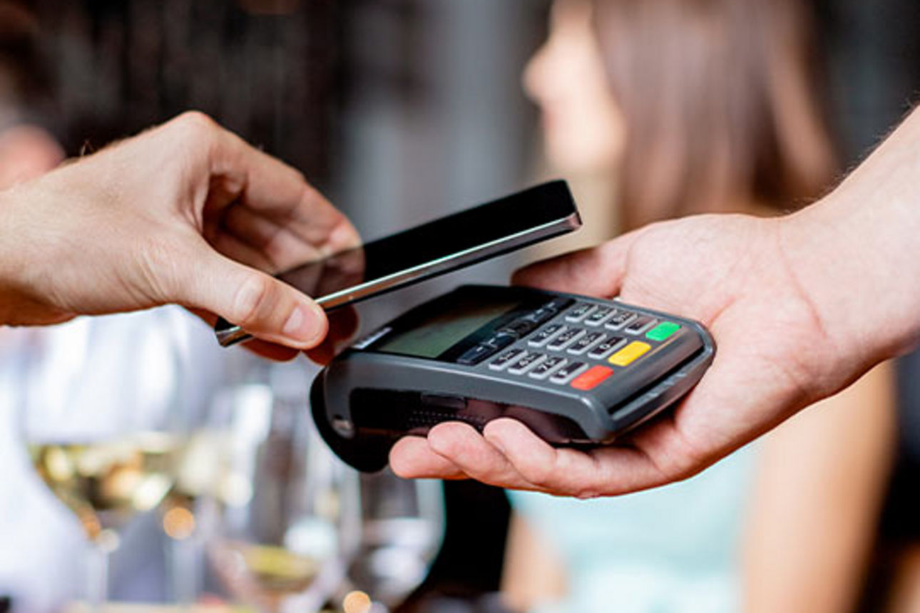 Ein Mann führt sein Smartphone über ein Cashgerät, um seine Getränke zu bezahlen.