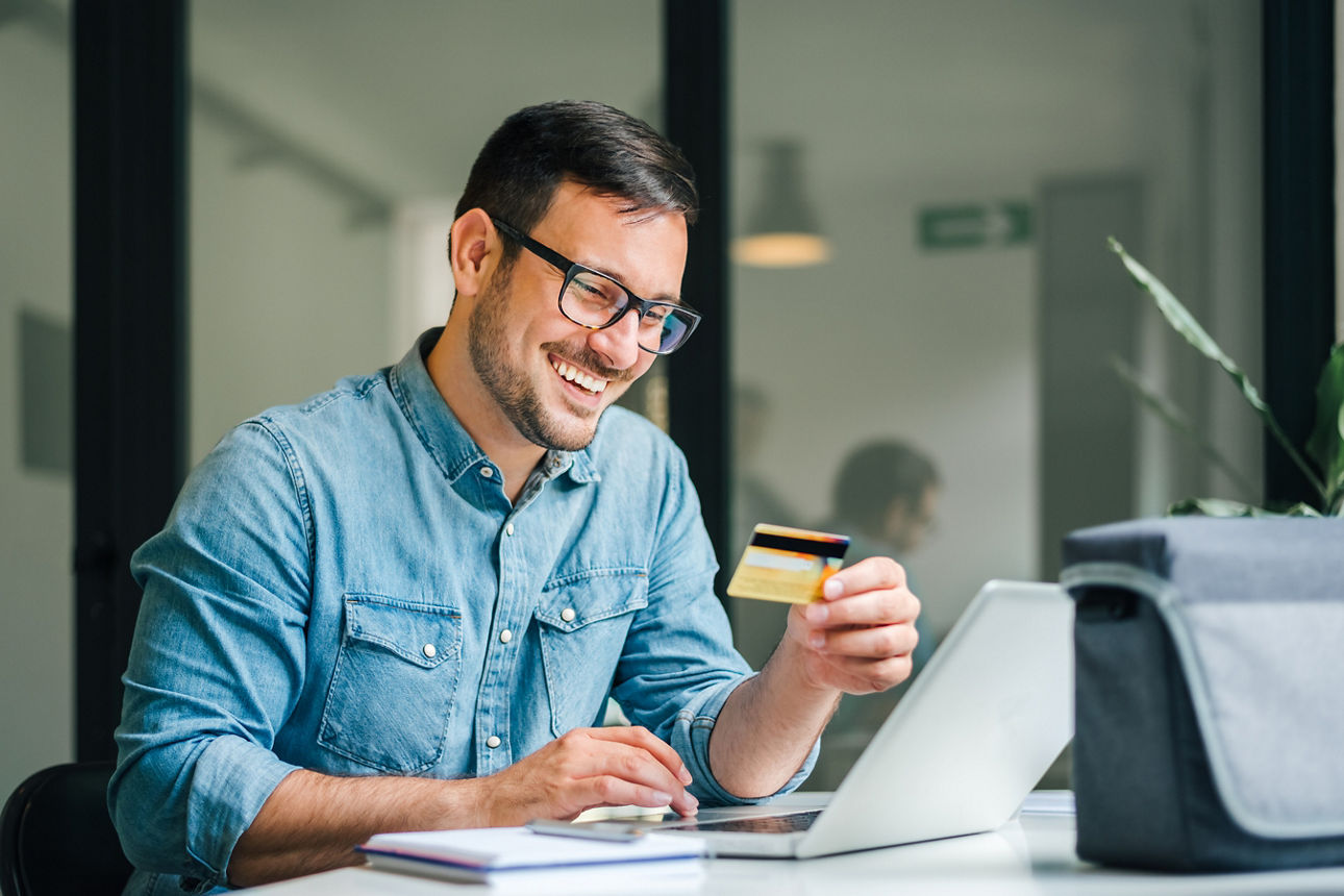 Ein Mann blickt lächelnd auf seine goldene Kreditkarte. 