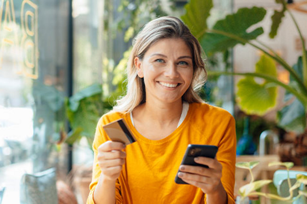 Eine Frau hält in der linken Hand eine Kreditkarte und in der rechten Hand ein Smartphone