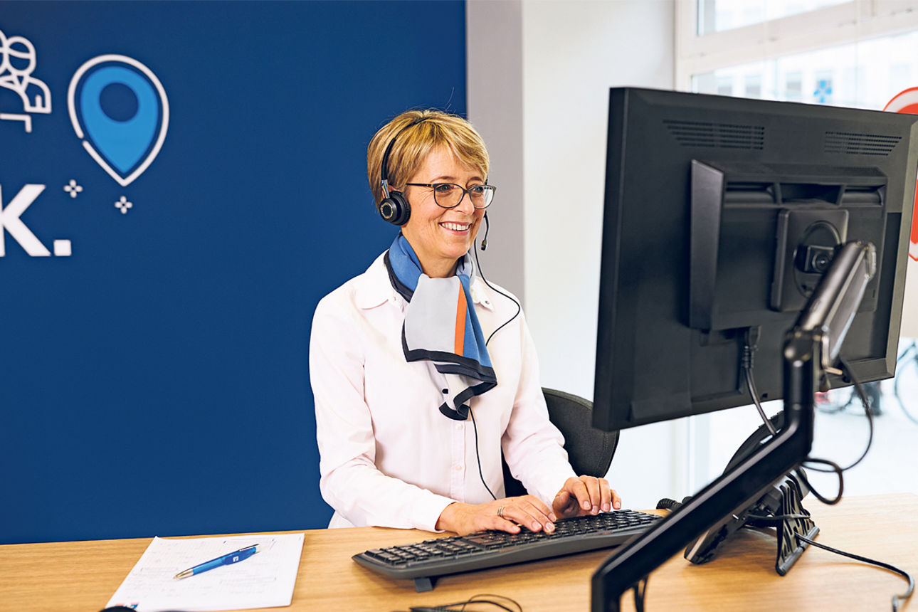 Beraterin mit Headset vor einem Computer in einer Bankfiliale