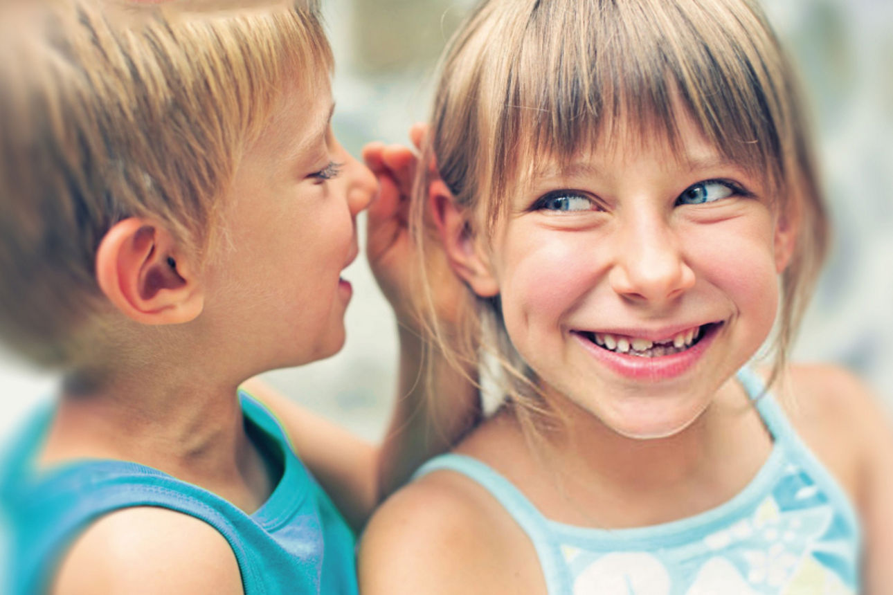 Ein Junge flüstert einem Mädchen ins Ohr