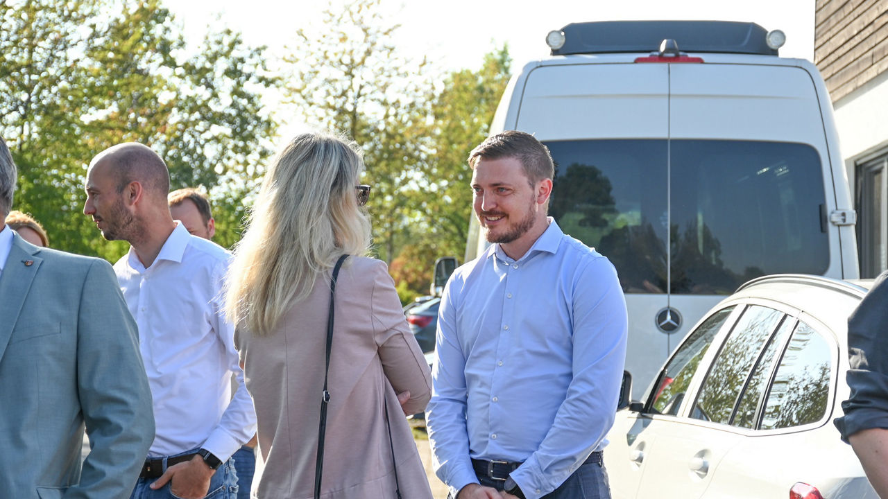 Geschäftsstellenleiterin Marina Finken unterhält sich mit einem Mitglied des Regionalbeirats auf einem Parkplatz mit Bäumen