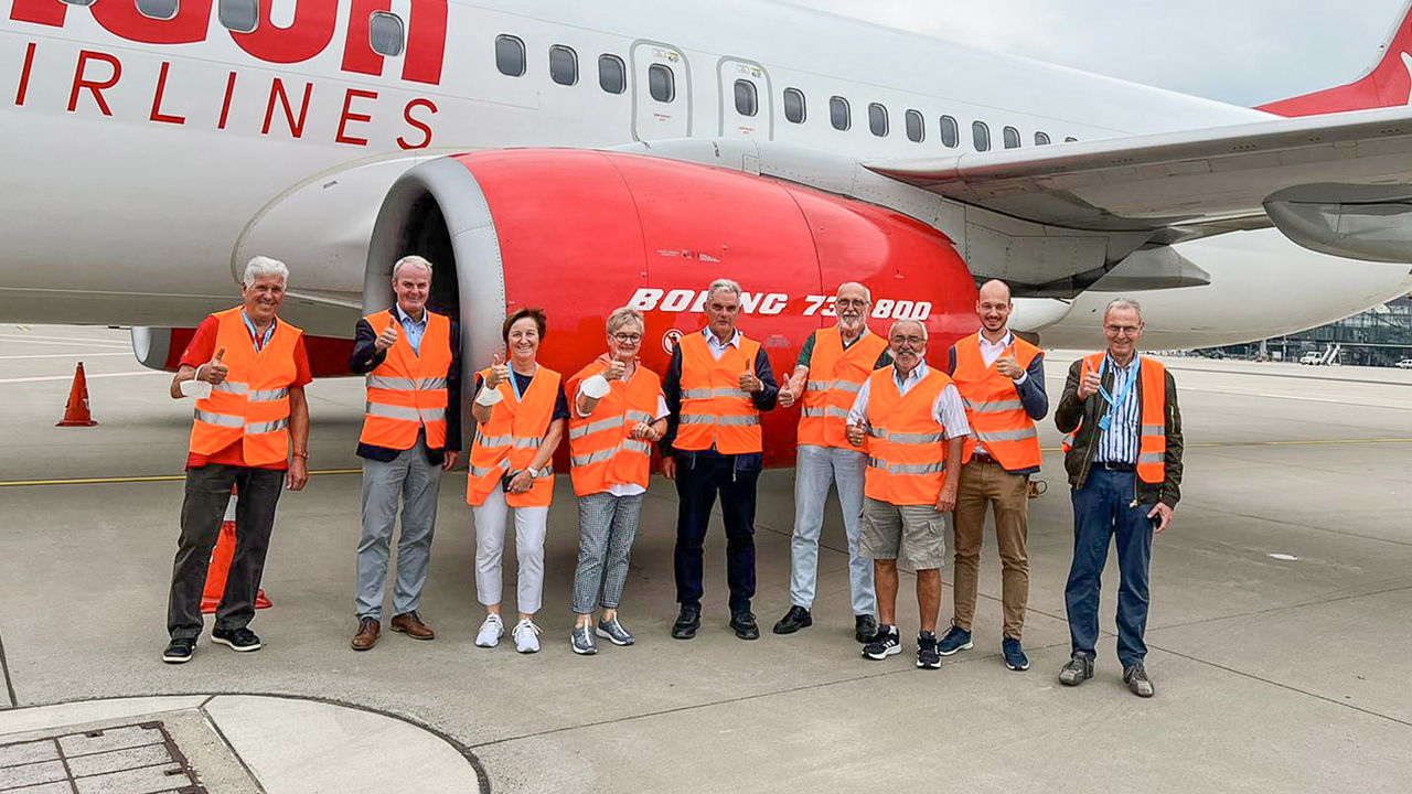 Mitglieder des Kundenbeirats stehen mit Warnwesten vor einem Flugzeug in der Nähe des Triebwerks und halten die Daumen hoch