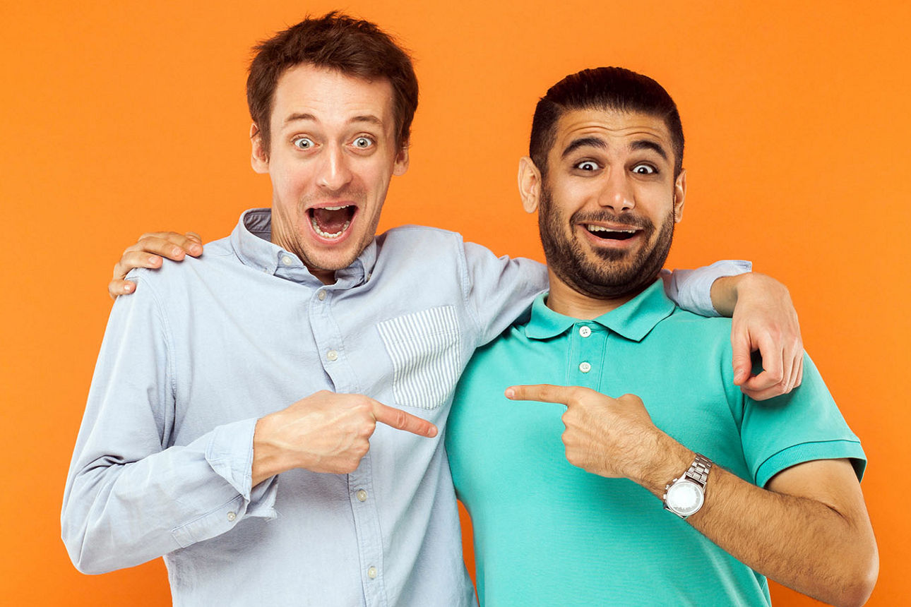 Zwei beste Freunde, umarmen, schockierte Fingerzeig einander und Blick in die Kamera mit Gesicht