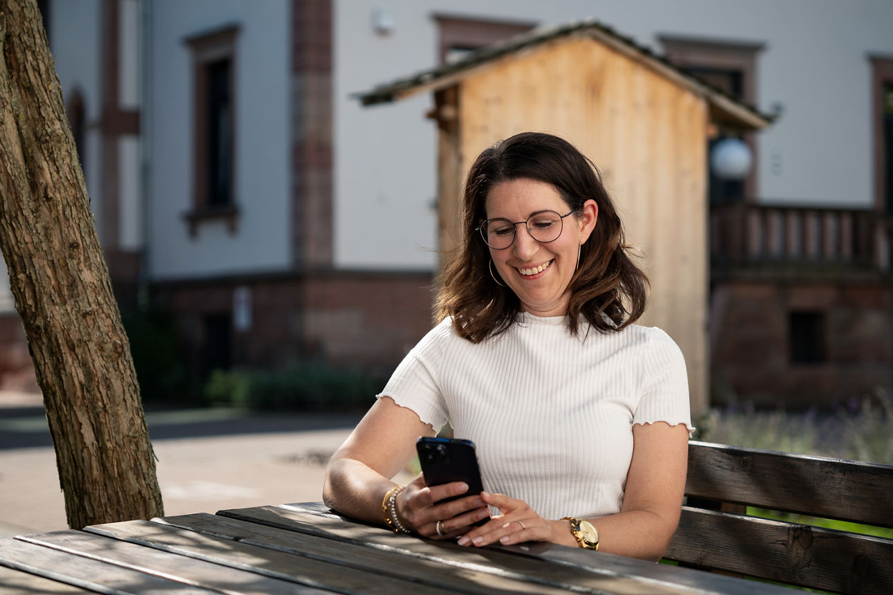 Eine Frau sitzt draußen lächelnd am Handy