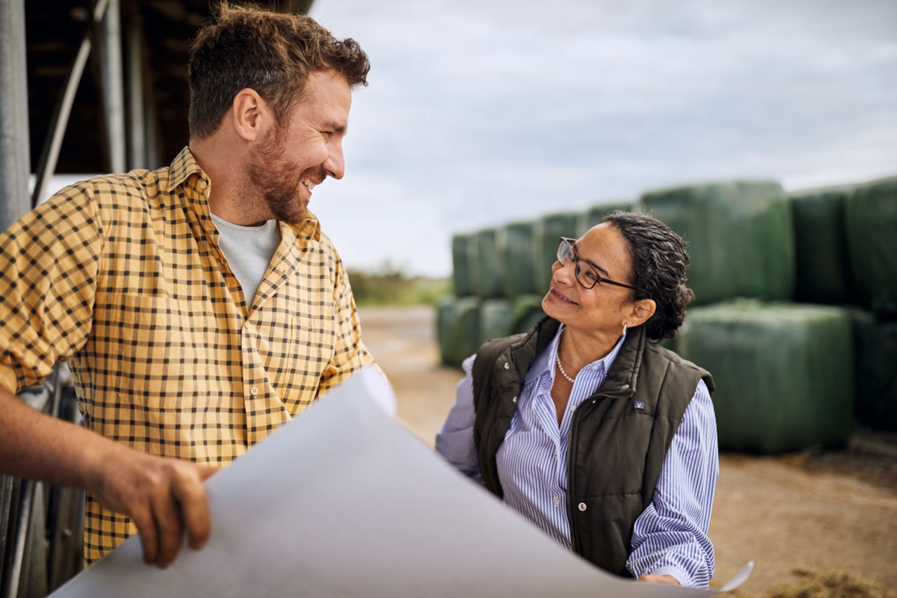 Ein Landwirt unterhält sich mit einer Dame und sie halten einen Plan in den Händen