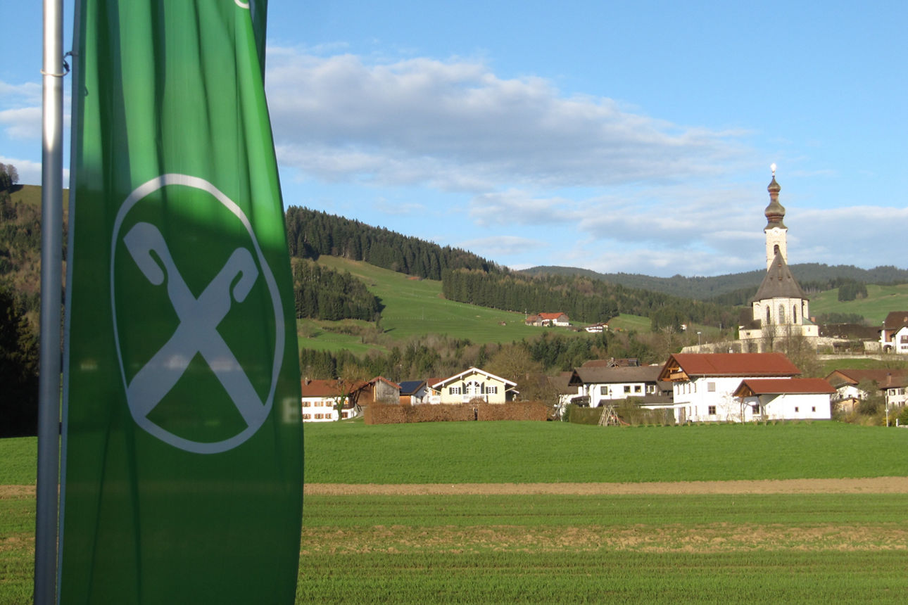 Das Bild zeigt eine ruhige Landschaftsszene unter einem hellen, teilweise bewölkten Himmel und einer grünen Flagge.