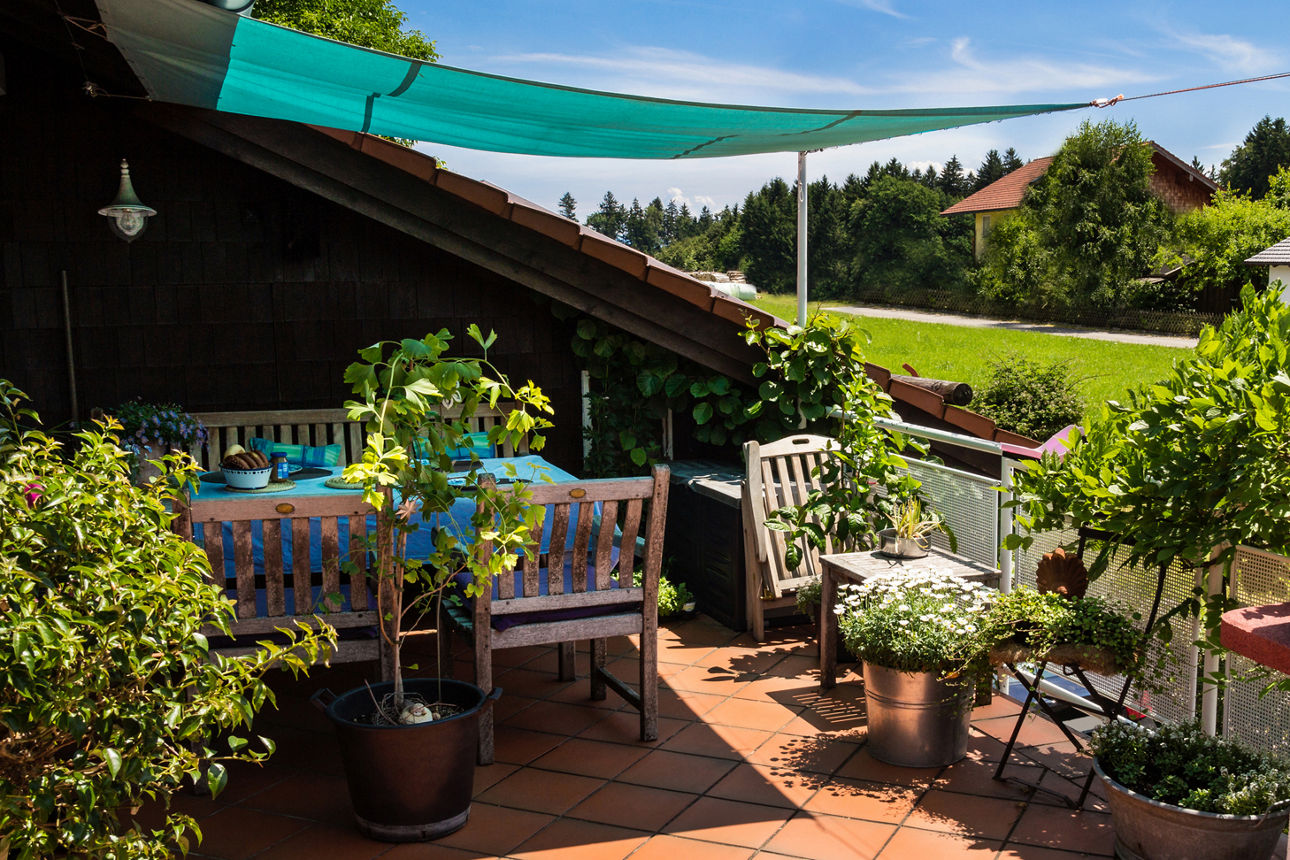 Patio mit vielen Grünpflanzen, Stühlen und einem Grill.