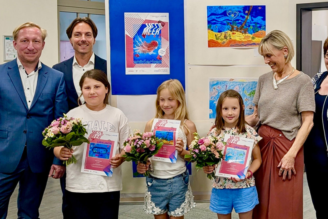 Kinder präsentieren stolz ihre Kunstwerke, begleitet von Erwachsenen im Ausstellungsraum.
