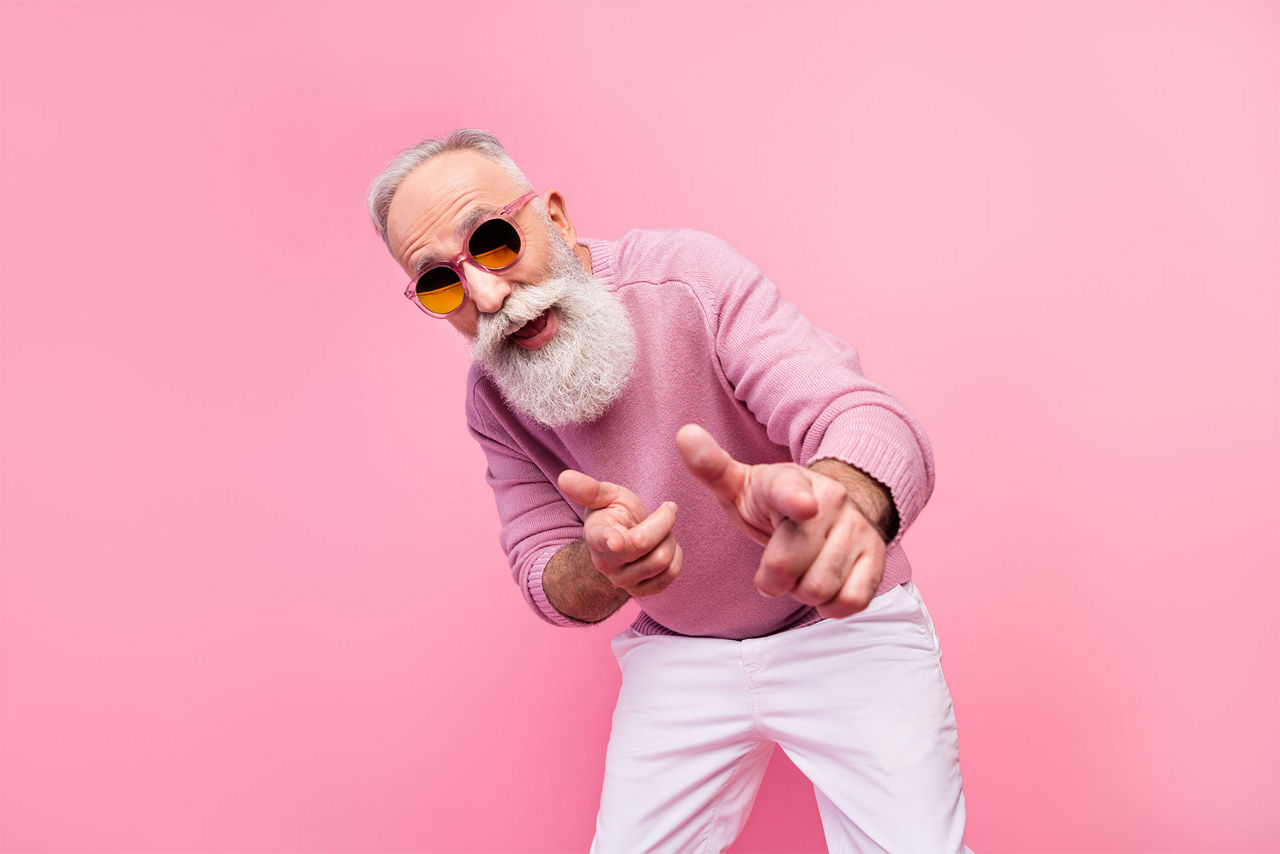 Älterer Mann vor einer rosa Wand mit rosa Pullover und Sonnenbrille