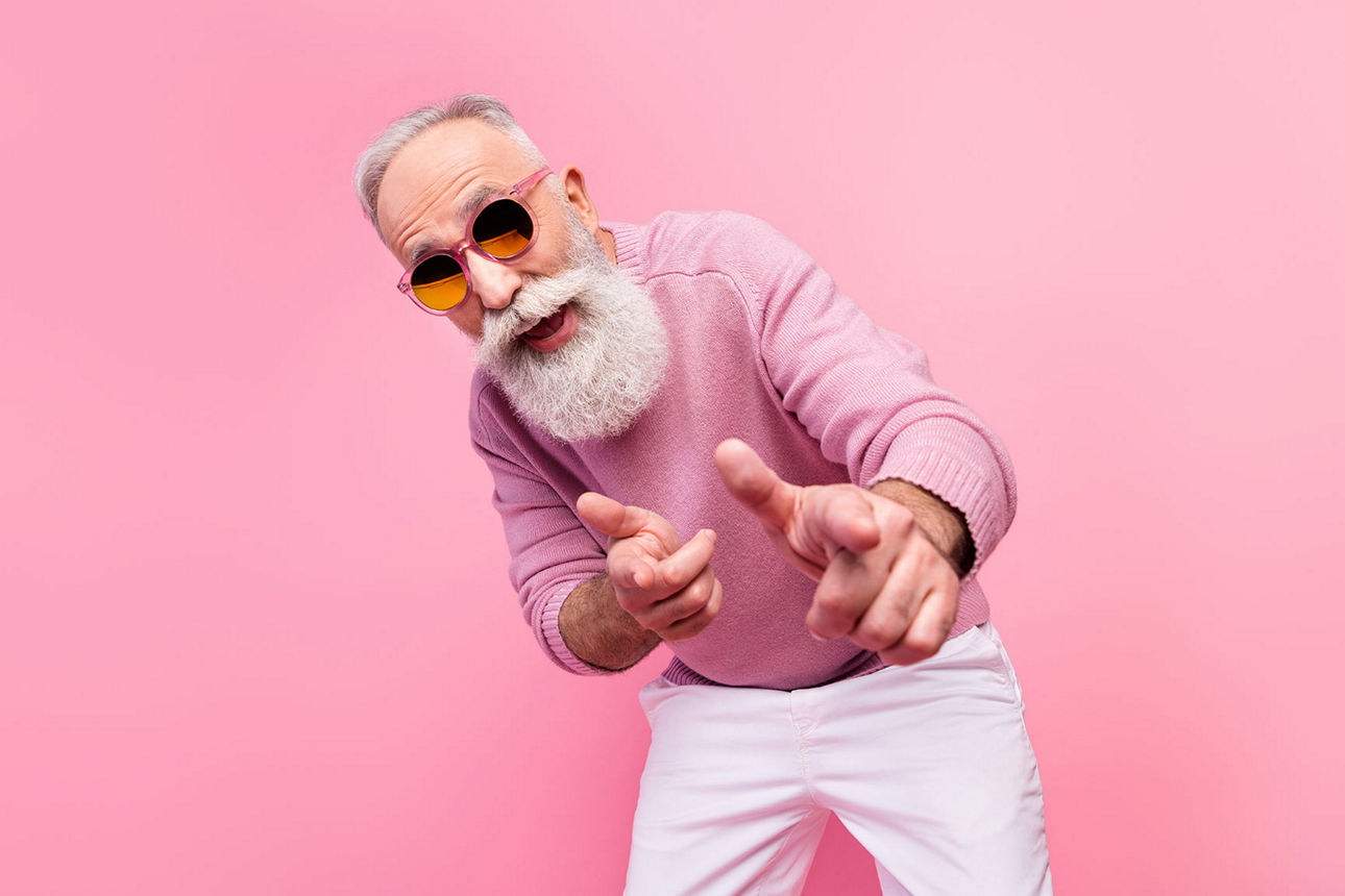 Älterer Mann vor einer rosa Wand mit rosa Pullover und Sonnenbrille