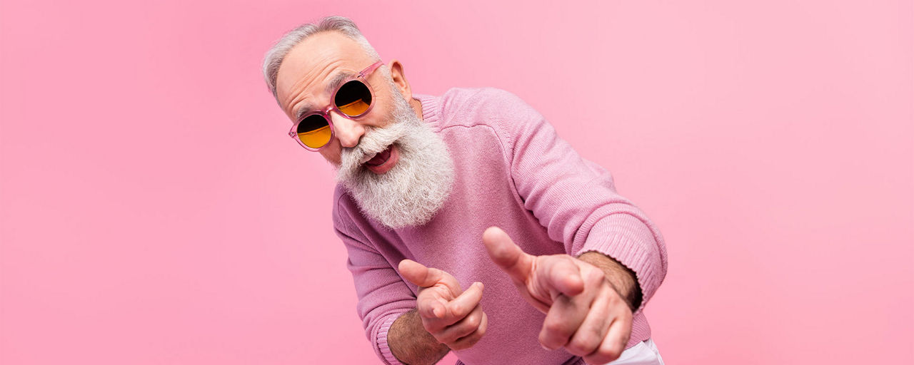 Älterer Mann vor einer rosa Wand mit rosa Pullover und Sonnenbrille