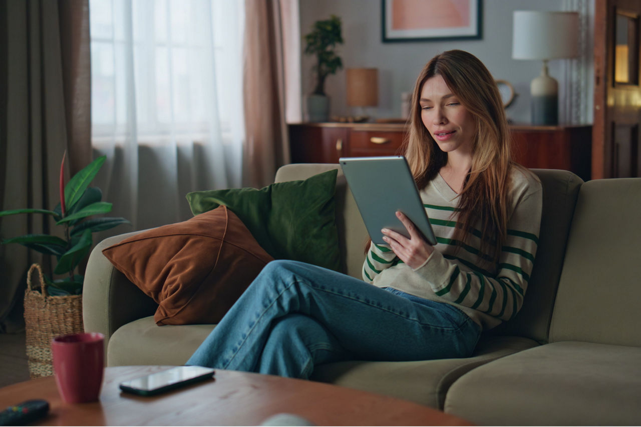 Junge Frau mit Tablet sitzt auf einer Couch