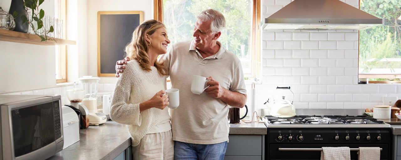 Glückliches älteres Paar steht in einer Küche mit einer Tasse in der Hand