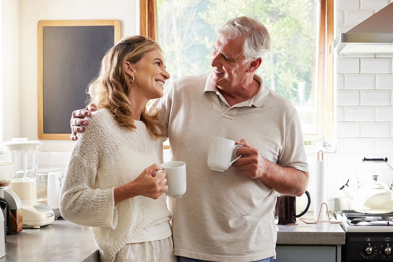Glückliches älteres Paar steht in einer Küche mit einer Tasse in der Hand