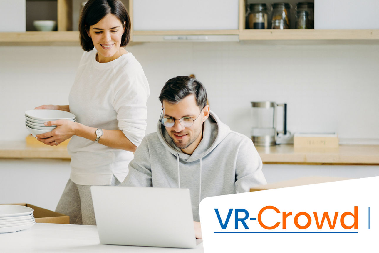 Junger Mann, der an einem Tisch sitzt und junge Frau, die dahinter steht, schauen auf einen Laptop