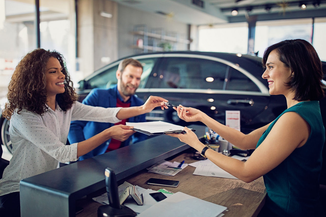 Pärchen unterschreibt in einem Autohaus ihren Leasingvertrag für ihr neues Fahrzeug bei der Automobilkauffrau