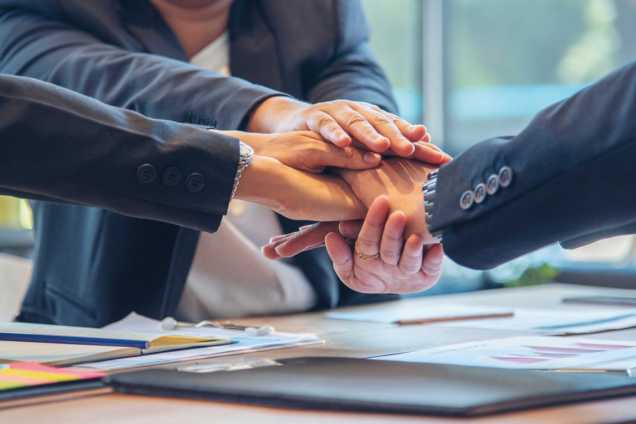 Mehrere Personen legen ihre Hände übereinander über einem Tisch mit Unterlagen und Stiften.