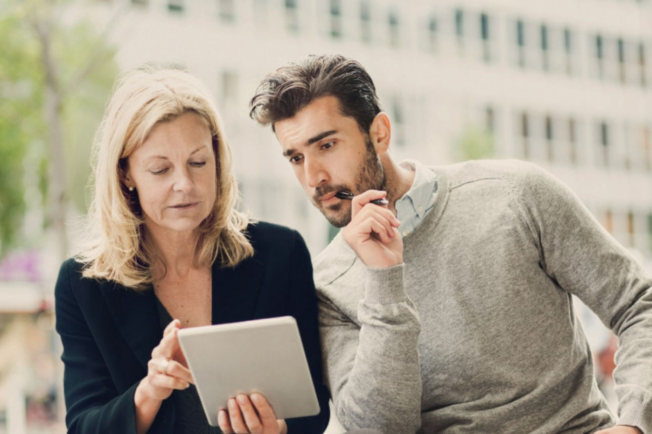 Ältere Frau und junger Mann blicken auf Tablet