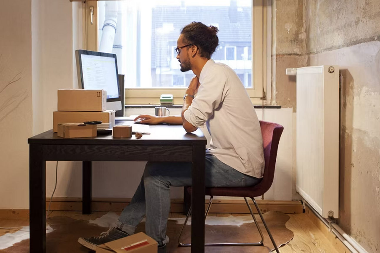 Mann in einem Raum sitzt an seinem Schreibtisch und schaut in seinen Rechner
