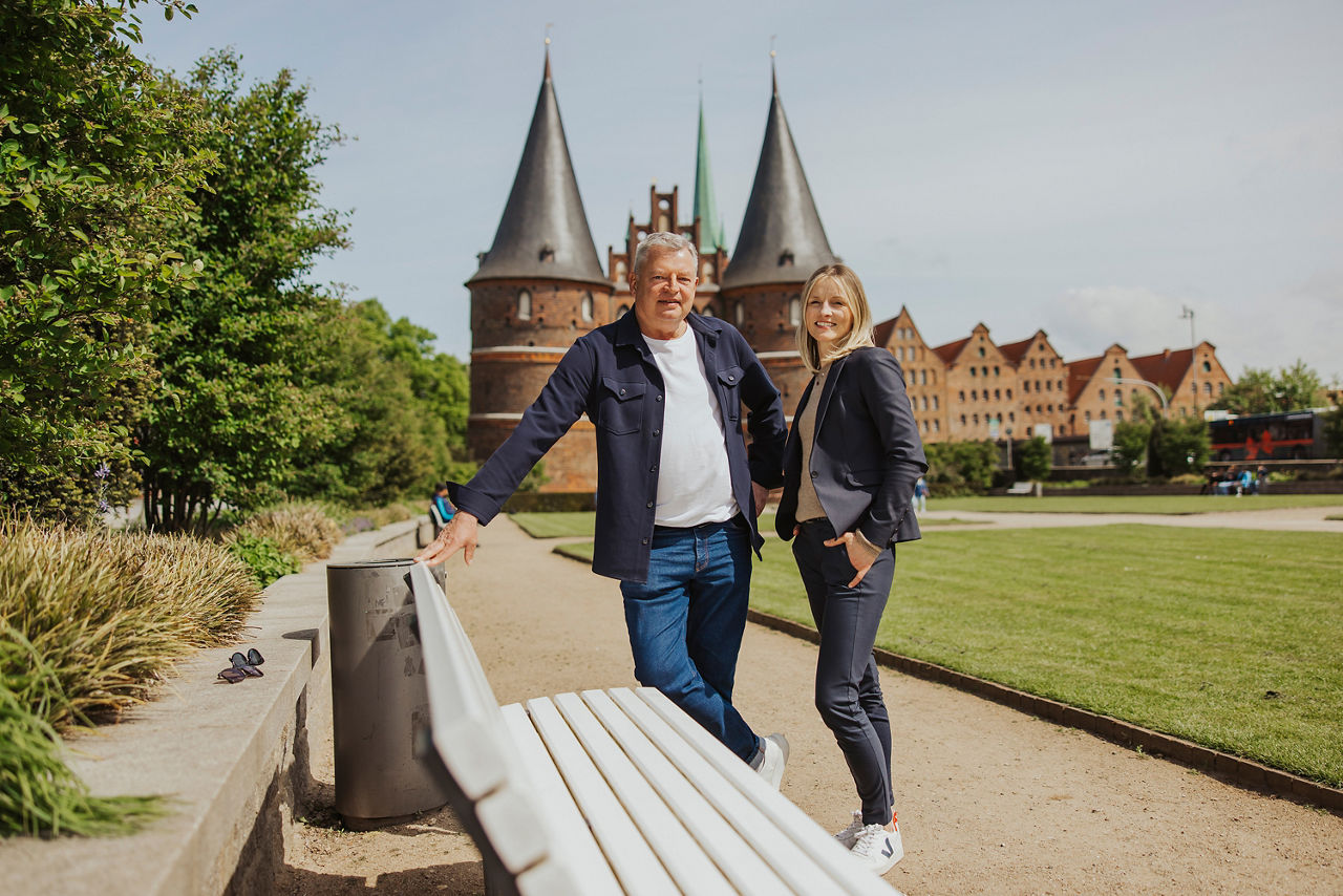 Ein Mann und eine Frau lächeln in die Kamera, während sie vor einer Backsteinburg stehen 