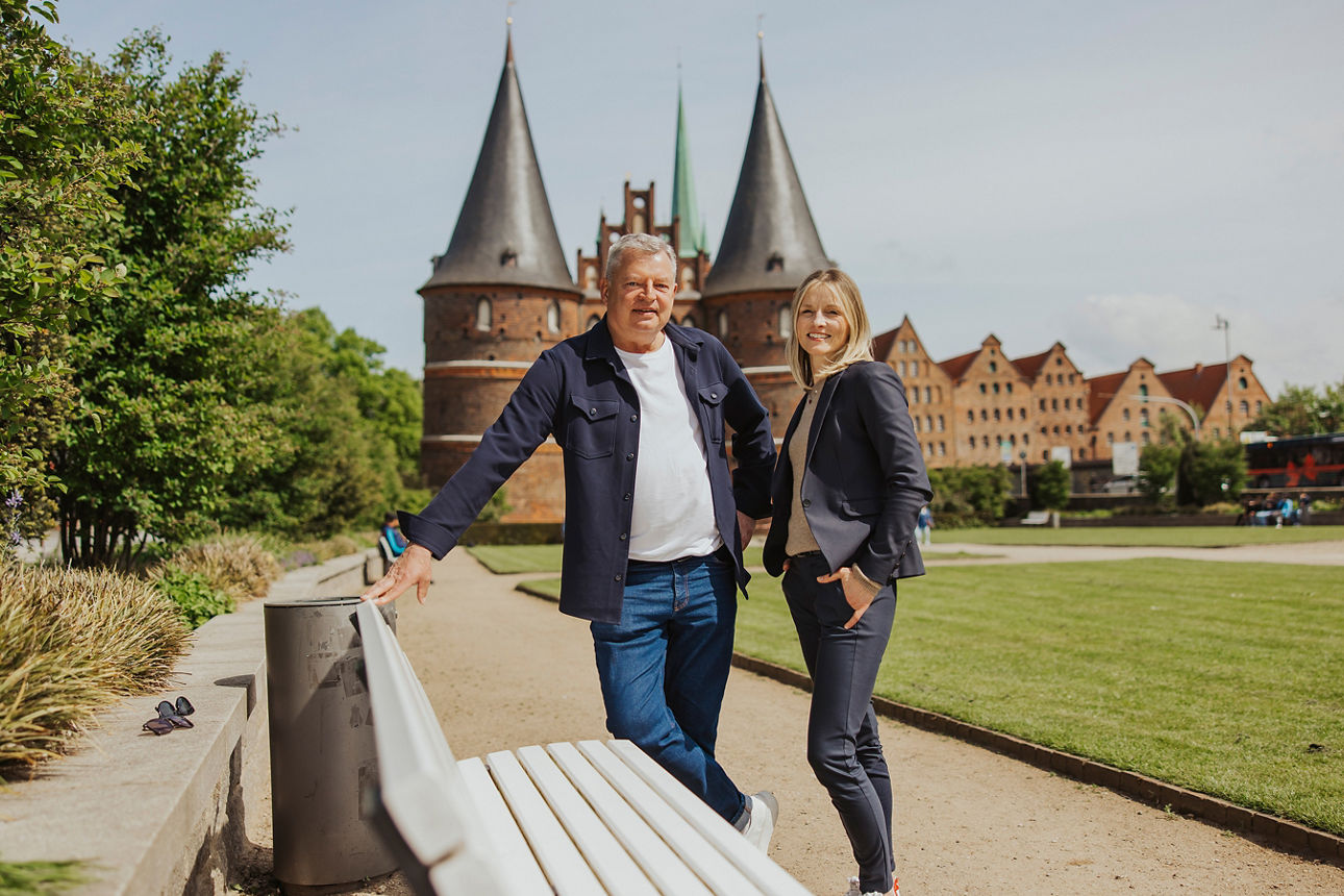 Ein Mann und eine Frau lächeln in die Kamera, während sie vor einer Backsteinburg stehen 