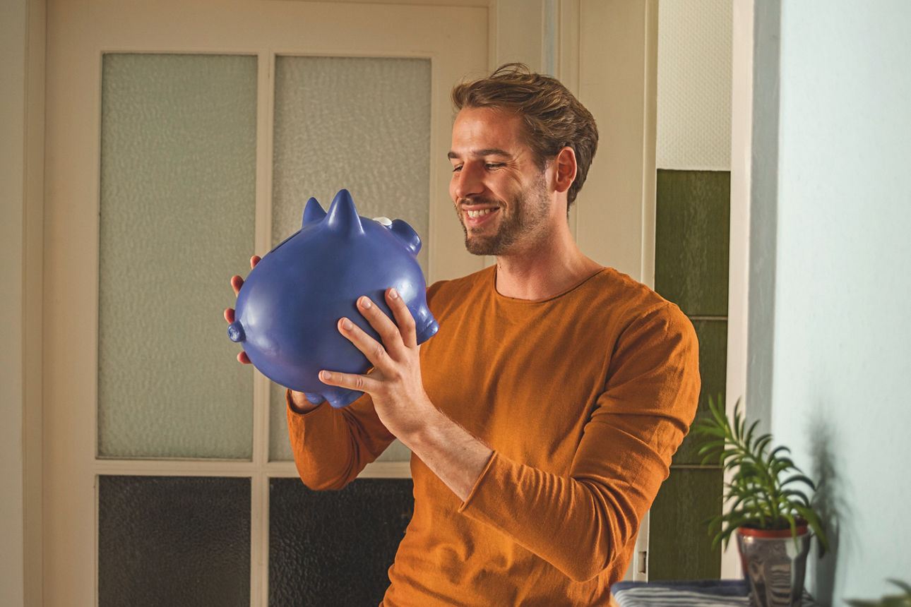 Ein Mann hebt ein großes blaues Sparschwein hoch