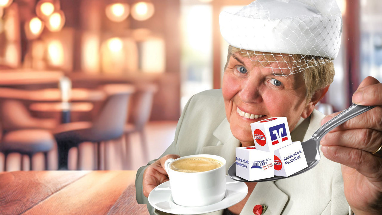 Margot Hinrichsen mit Kaffeetasse und Raiffeisenwürfel auf Löffel anstelle von Zuckerwürfeln