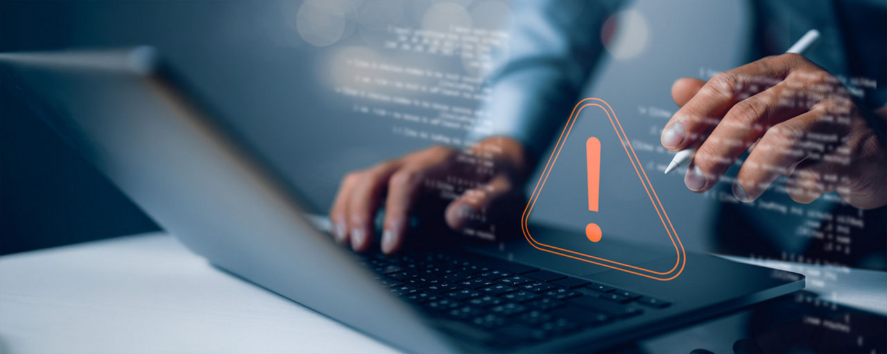 Hände an einem Laptop mit einem Achtung-Icon