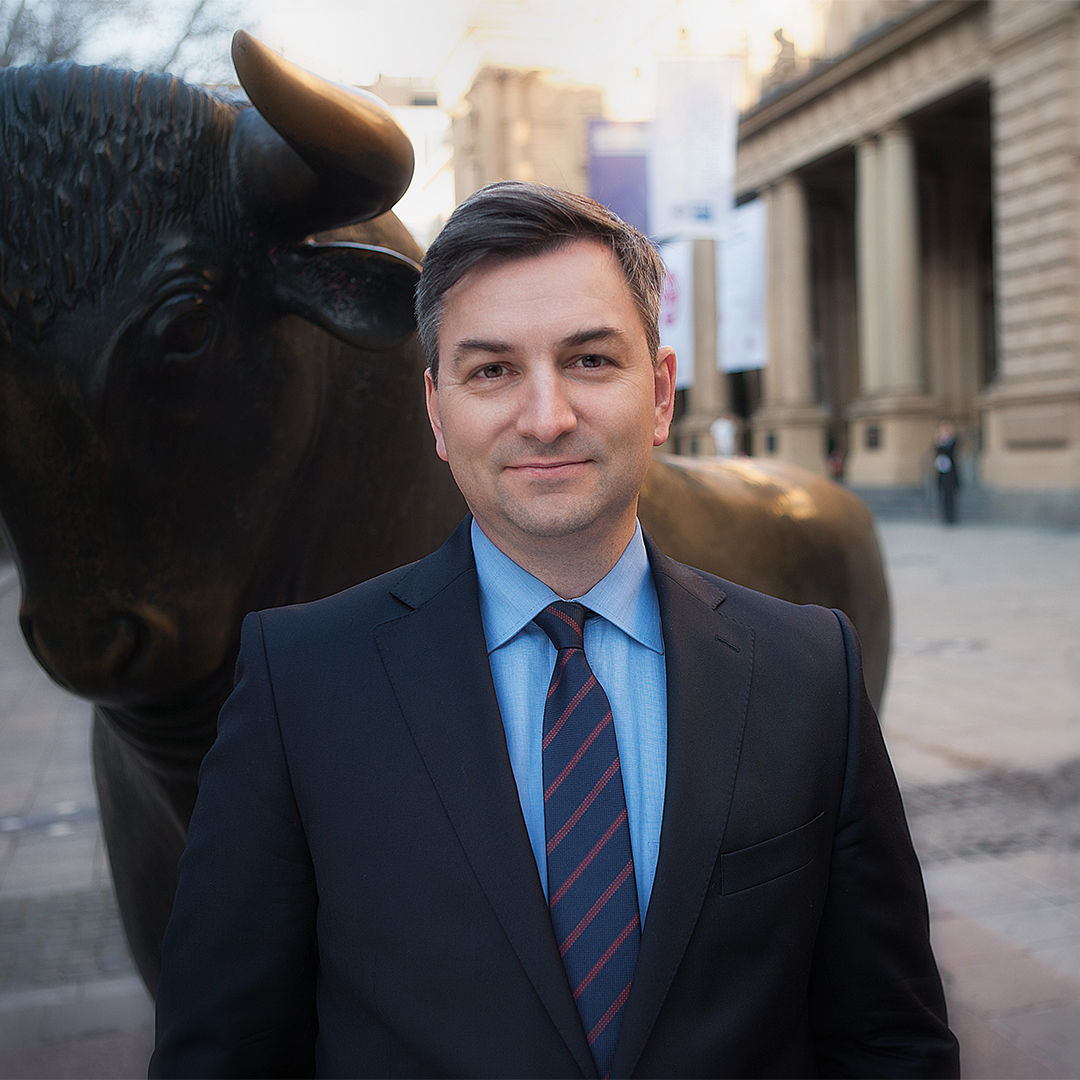 Markus Gürne steht mit Anzug und Krawatte vor dem Bullen an der Frankfurter Börse