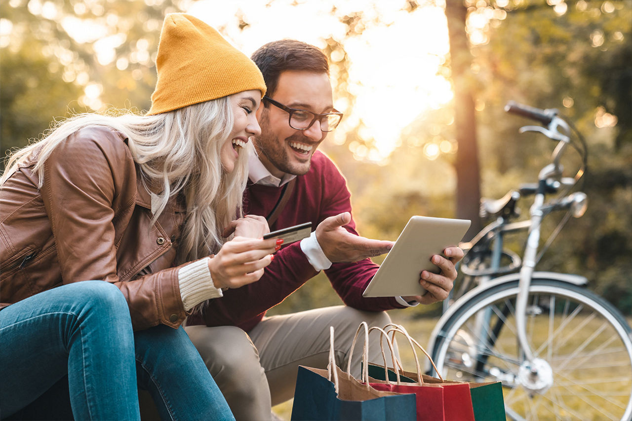 Pärchen sitzt mit Tablet und Kreditkarte in der Natur.
