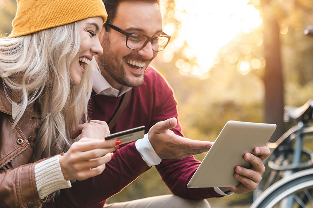 Pärchen in der Natur mit Karte und Tablet beim Online-Shopping.