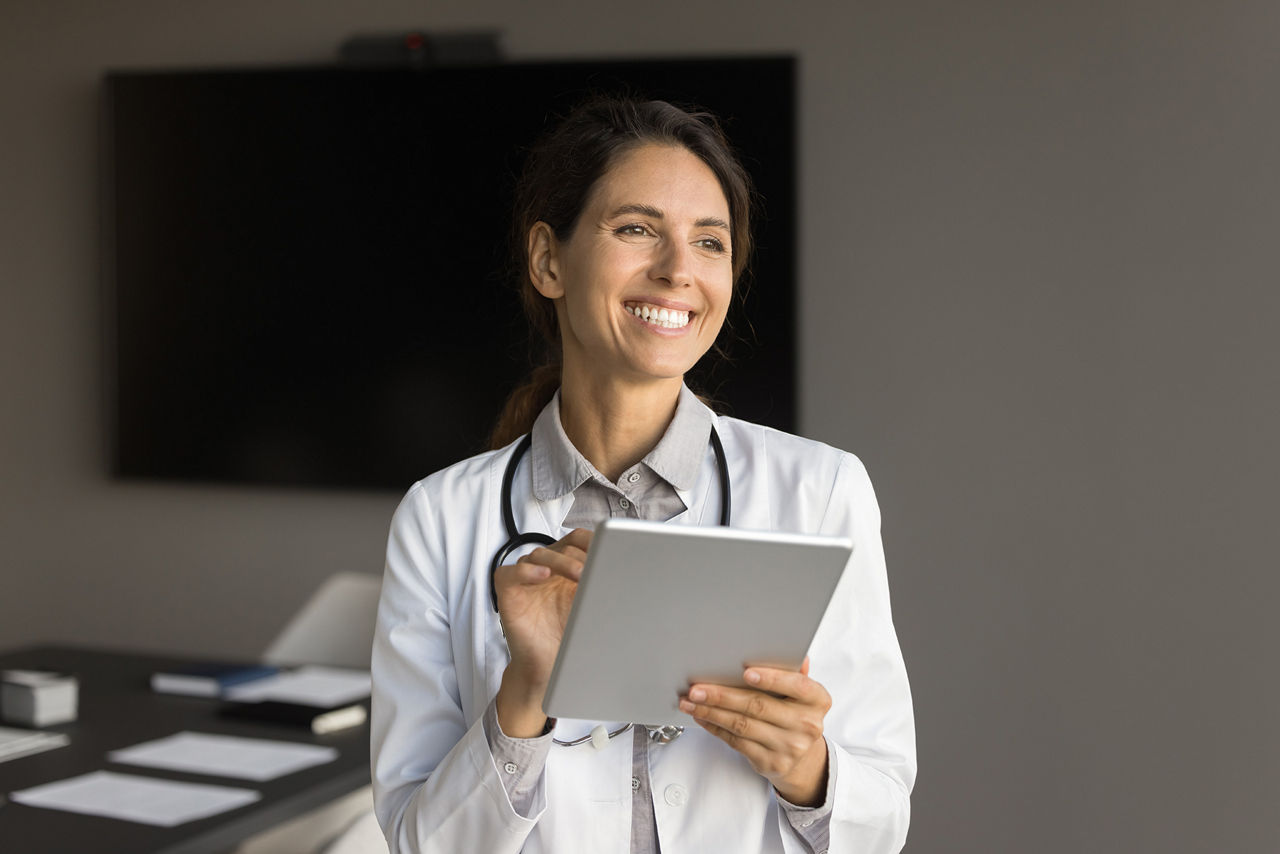 Lächelnde junge Ärztin im Büro hält ein Tablet in der Hand.
