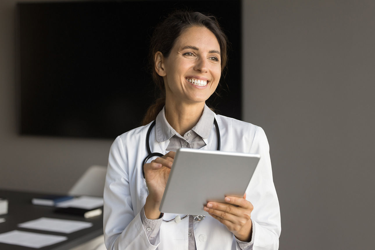 Lächelnde junge Ärztin im Büro hält ein Tablet in der Hand.