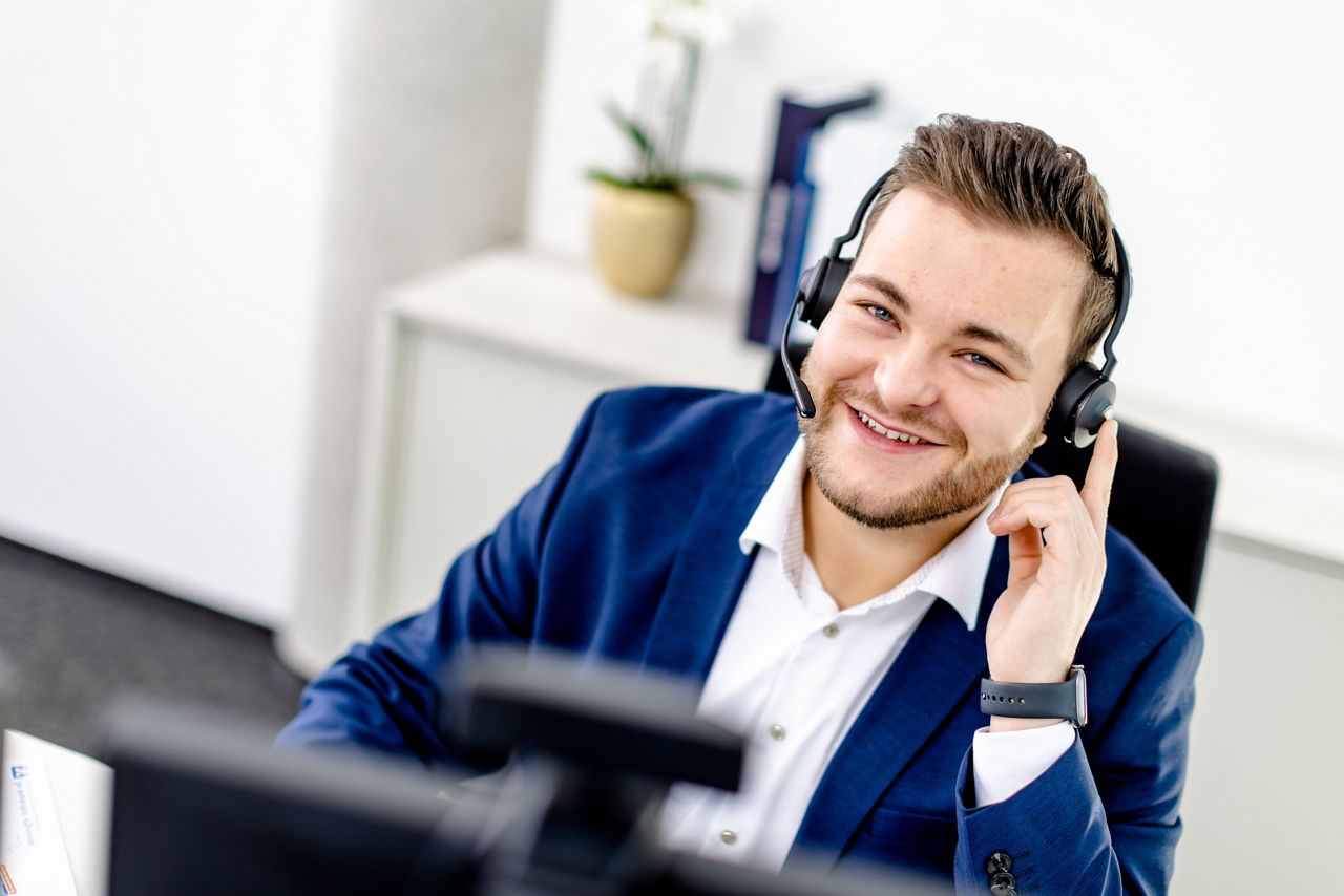 ein lächelnder Mann, der ein Headset und einen blauen Blazer trägt.